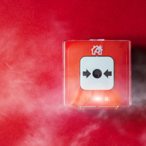 Fire alarm system on a wall surrounded by smoke on a red background with copy space. Pull danger fire safety box. Break red alarm equipment detector safe detector.