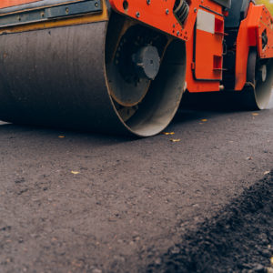 Workers operating asphalt paver machine during road construction. Close view on the road roller working on the new road construction site.